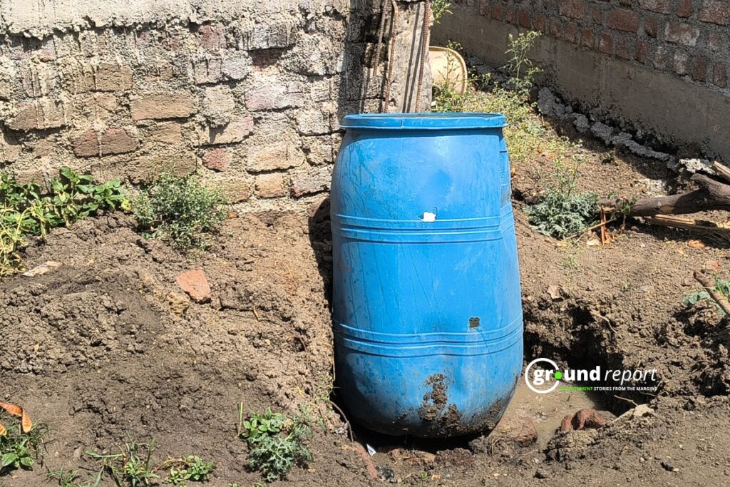 A blue plastic drum buried in the ground, likely used to store or collect water.