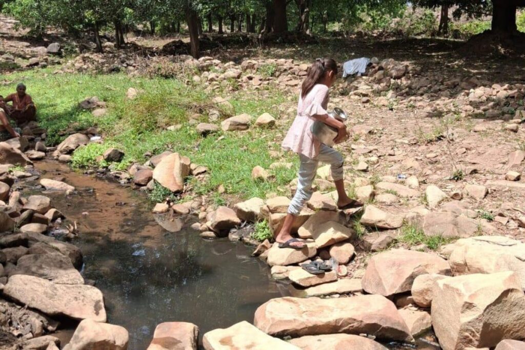 A teenage girl from the Kol community crosses a rocky stream to fetch water in water-scarce Chitrakoot.