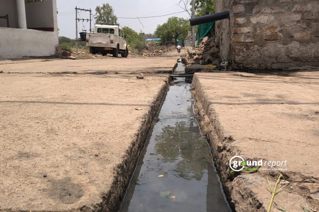 Dirty water flows through an open drain running down the middle of the village street.