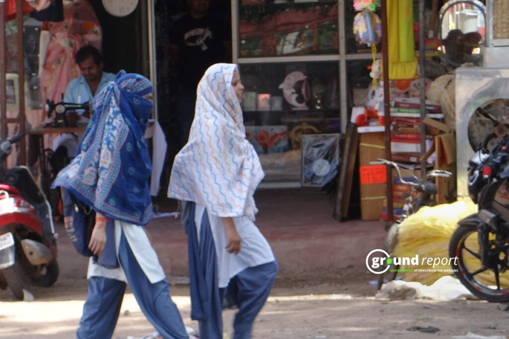 Two women cover their heads and faces with scarves as they walk past a shop during peak heat hours.