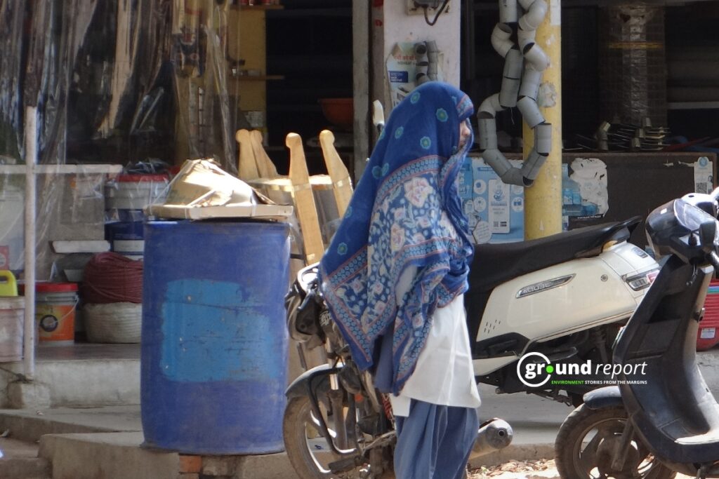 A woman pulls a scarf over her face to block the sun as she walks through a market area.