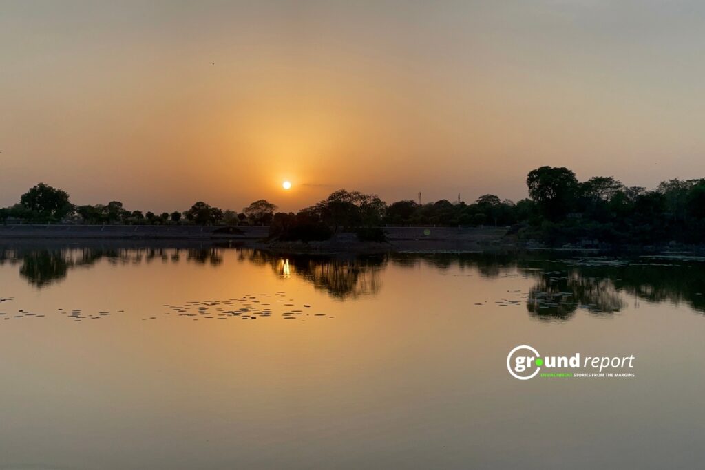 The sun sets over a lake, its light reflecting on the still water.