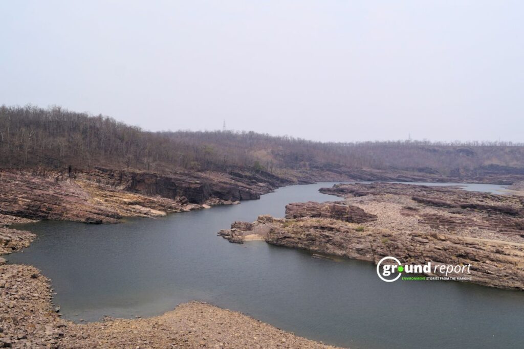 A dry, rocky stretch of the Narmada shows low water levels and stressed surroundings.
